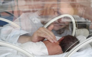 Una mujer toca a un bebé en una incubadora neonatal; solo un ejemplo de plástico de policarbonato en dispositivos médicos.