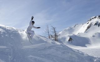 Un practicante de snowboard con traje de nieve blanco y casco negro desciende de una montaña.